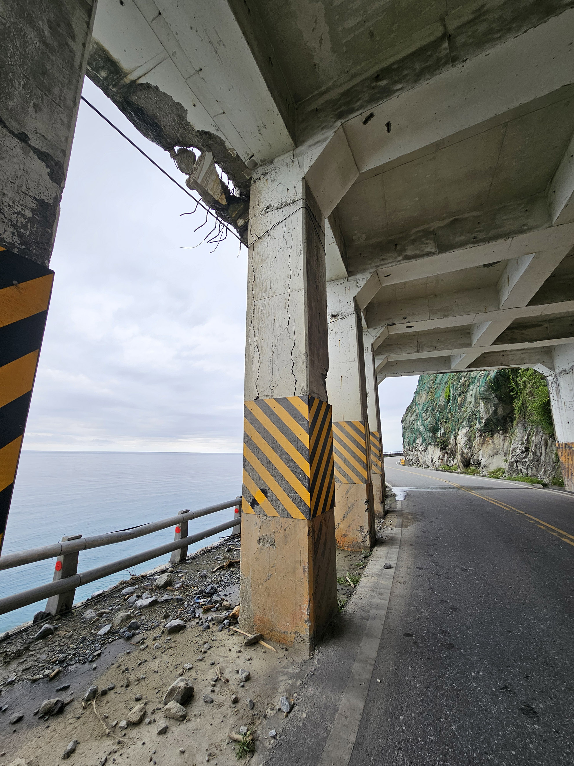 pare-bloc en béton, lors du séisme, des blocs sont venus l'impacter. Ici gros plan sur un impact en rive de pare-bloc ce qui a créé une rupture de la dalle mais aussi une fissuration verticale du poteau par sur-compression